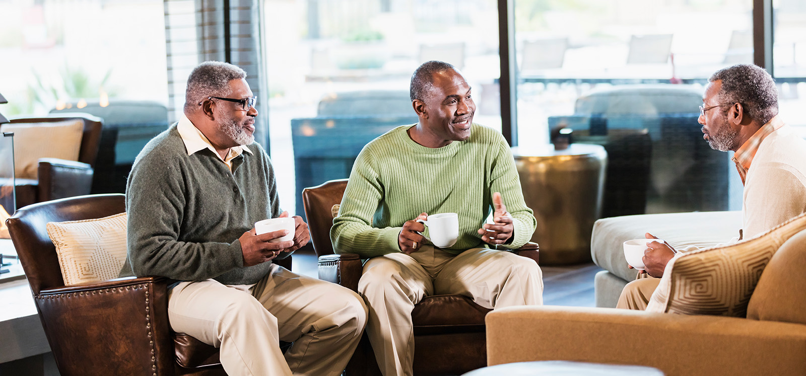 Three mature African-American men sitting in a lounge conversing, drinking coffee.