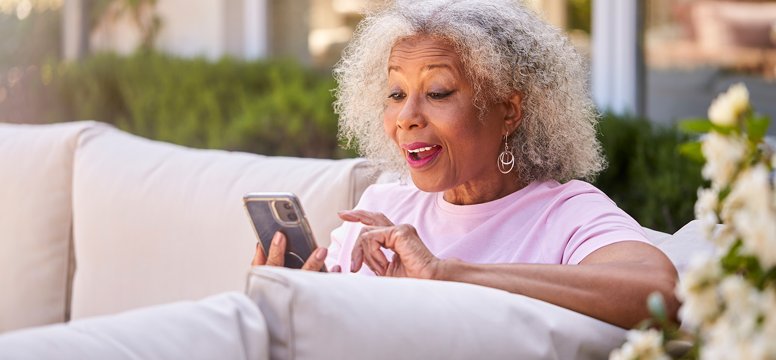 Senior Retired Woman Sitting Outside In Garden At Home Making Video Call On Mobile Phone