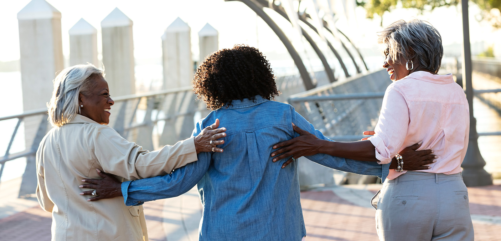 Rear view of a group of three senior African-American women, best friends, hanging out together on a sunny day on a city waterfront, on a pedestrian walkway.